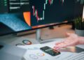 A person analyzing cryptocurrency charts on a computer with a legal document in focus.