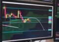 A digital screen displaying cryptocurrency prices and trading charts in a trading room.