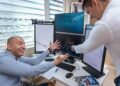 People celebrating in an office while analyzing financial graphs on screens.
