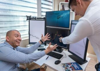 People celebrating in an office while analyzing financial graphs on screens.