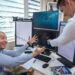 People celebrating in an office while analyzing financial graphs on screens.