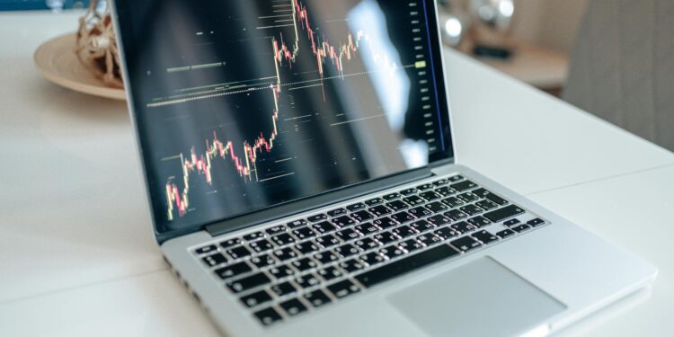 A financial analyst examines cryptocurrency charts on a laptop in a modern office setting.