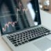 A financial analyst examines cryptocurrency charts on a laptop in a modern office setting.