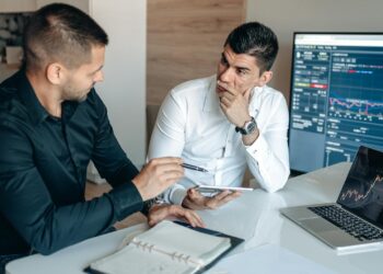 Investors discussing cryptocurrency in a modern office setting, charts and laptops visible.