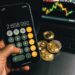 A hand holds a smartphone displaying various cryptocurrency logos against a backdrop of UK government buildings.