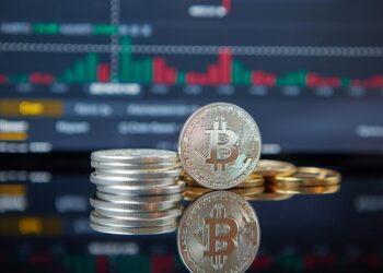 Bitcoin coins stacked with a fluctuating stock market graph in the background.