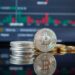 Bitcoin coins stacked with a fluctuating stock market graph in the background.