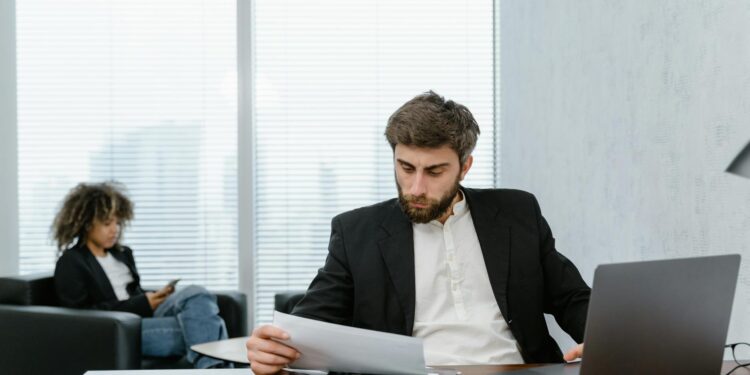 Retired man looking distressed while reviewing financial documents and a laptop with crypto data.