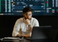 A developer analyzing blockchain data on a laptop with cryptocurrency graphics in the background.