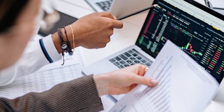 Two professionals discussing a document with cryptocurrency charts and financial data on a screen.