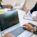A business professional analyzes cryptocurrency charts on a laptop with financial documents nearby.