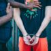 A person in handcuffs being led away by law enforcement, with financial documents visible.