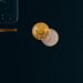 A stack of coins with Bitcoin and Ethereum logos beside a calculator and financial documents.
