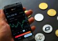 G. Love holds a smartphone showing a fake Ledger app with Bitcoin graphics in the background.