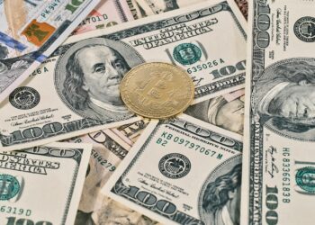 Digital currency symbols with a background of US dollar bills and a warning sign.