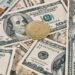 Digital currency symbols with a background of US dollar bills and a warning sign.
