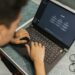 A developer using a laptop with blockchain graphics, showcasing Certik's AI Auditor tool.