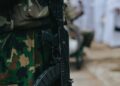 Soldiers on a military base, some carrying firearms, discussing new firearm policy.
