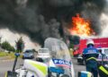 Flames engulf a luxury home, police cars surrounding the scene after a firebomb attack.