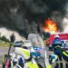 Flames engulf a luxury home, police cars surrounding the scene after a firebomb attack.
