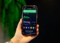 A person holds a smartphone displaying a Polymarket screen amid financial news articles.