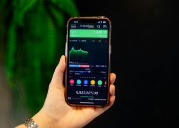 A person holds a smartphone displaying a Polymarket screen amid financial news articles.