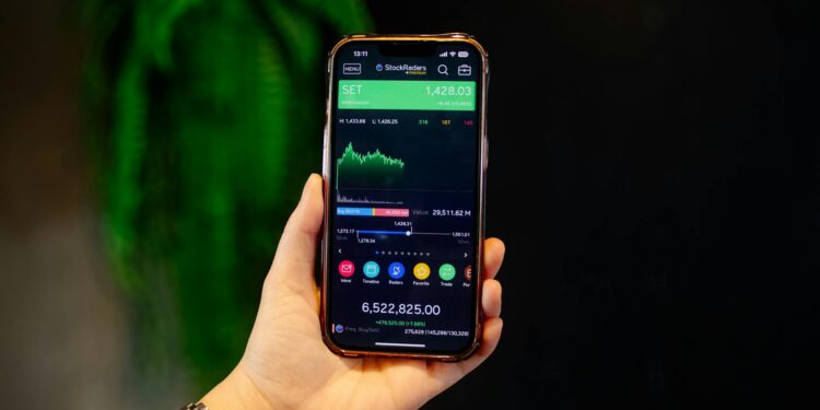 A person holds a smartphone displaying a Polymarket screen amid financial news articles.