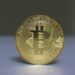A Bitcoin coin stands strong against oil barrels, symbolizing market resilience amidst Iran tensions.