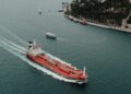 An oil tanker navigating the Strait, overlaid with Bitcoin and financial symbols.