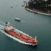 An oil tanker navigating the Strait, overlaid with Bitcoin and financial symbols.