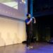 Justin Sun speaking at a conference with blockchain graphics in the background.