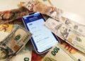 A smartphone displaying the Pix payment app alongside cash and international currency symbols.