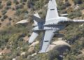 F-15E aircraft in flight over rugged terrain, with smoke rising from a distant location.