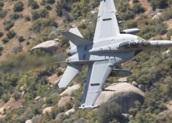 F-15E aircraft in flight over rugged terrain, with smoke rising from a distant location.