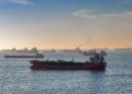 Oil tankers navigating the Strait of Hormuz with a Bitcoin symbol overlay representing taxation.