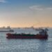 Oil tankers navigating the Strait of Hormuz with a Bitcoin symbol overlay representing taxation.