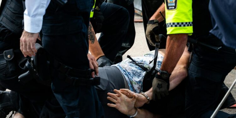 Benjamin Pasternak in handcuffs being led away by police officers at a courthouse.