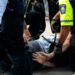 Benjamin Pasternak in handcuffs being led away by police officers at a courthouse.