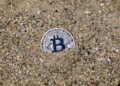 A stranded ship in the Strait of Hormuz with digital currency symbols overlayed.