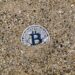 A stranded ship in the Strait of Hormuz with digital currency symbols overlayed.