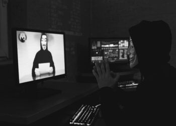 A hacker sitting at a computer with crypto-related graphics on the screen.