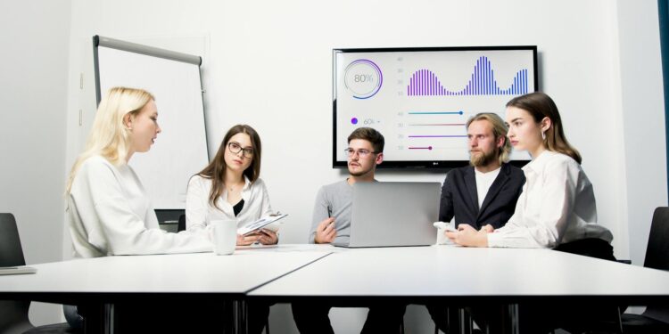 A corporate team celebrating in front of a digital display showing record valuations.