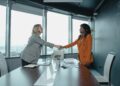 Payward CEO shaking hands with Bitnomial executives in a modern office setting.