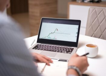 A person examines cryptocurrency charts on a computer screen in a modern office.