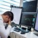Falling stock charts and a worried trader at a financial market desk during tense economic times.