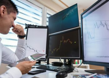 A trader monitors Bitcoin prices and oil market charts on multiple screens.