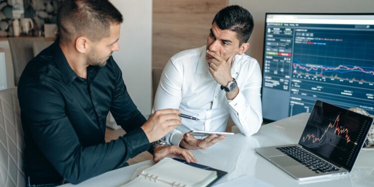 Traders examining financial charts with Bitcoin symbols and stock market screens in the background.