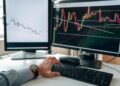 A trader analyzes Bitcoin charts on a computer screen with financial graphs in the background.