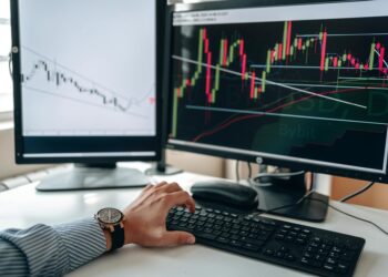 A trader analyzes Bitcoin charts on a computer screen with financial graphs in the background.