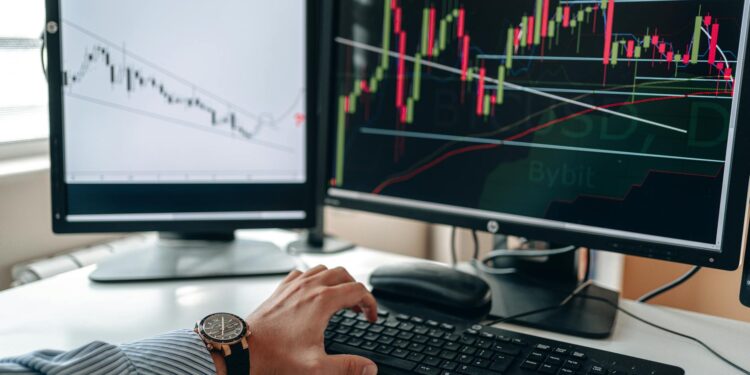 A trader analyzes Bitcoin charts on a computer screen with financial graphs in the background.